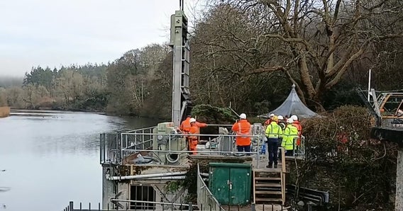 Workers in safety gear install Hydrolox water screen on the side of a river.