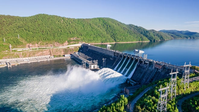 Dam on river with water flowing throw and verdant hill in background