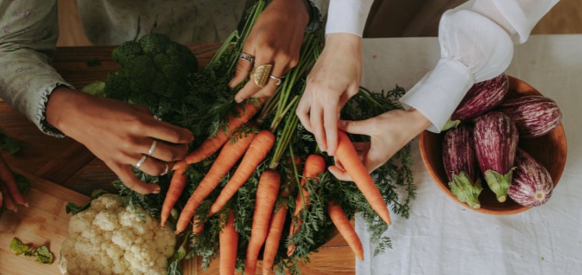 Two people sorting through a table of gut-friendly food, including carrots, cauliflower and eggplant.