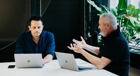 Two men talking with laptops in a digital agency