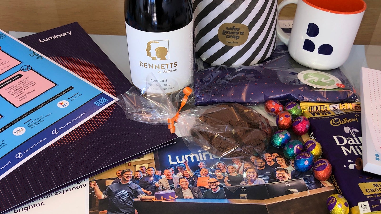 Care pack sent to Luminary staff, featuring chocolates, coffee cup, wine, notepad, values statement, toilet paper and mental health guidance sheet.