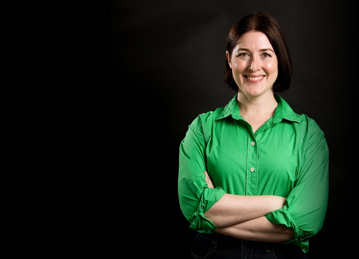 Picture of Luminary employee, Anna Potter smiling standing in front of a black screen in a green top