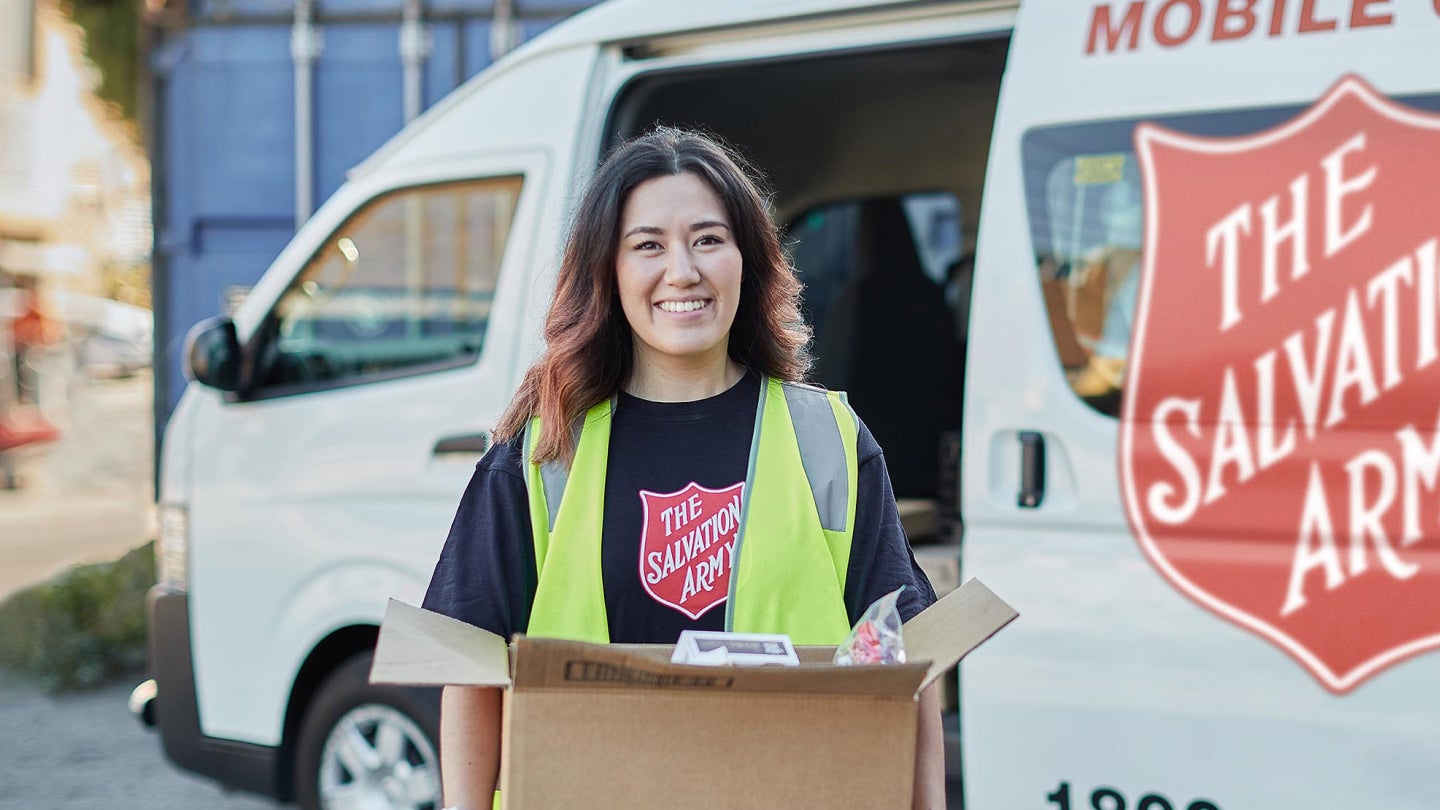 Woman in high vis vest standing with a box in front of a Salvos truck