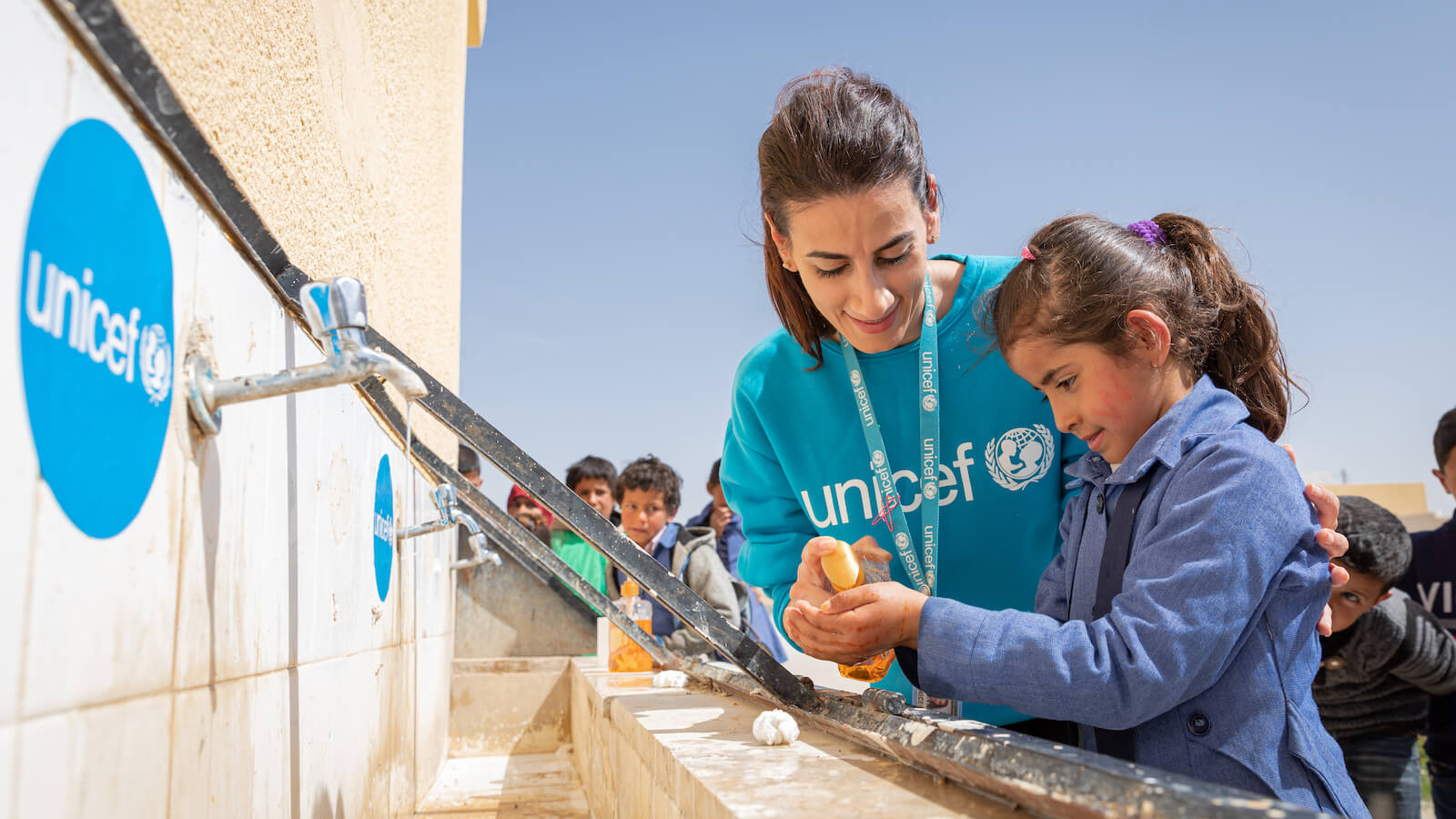 Image of a Unicef working helping a small girl with water