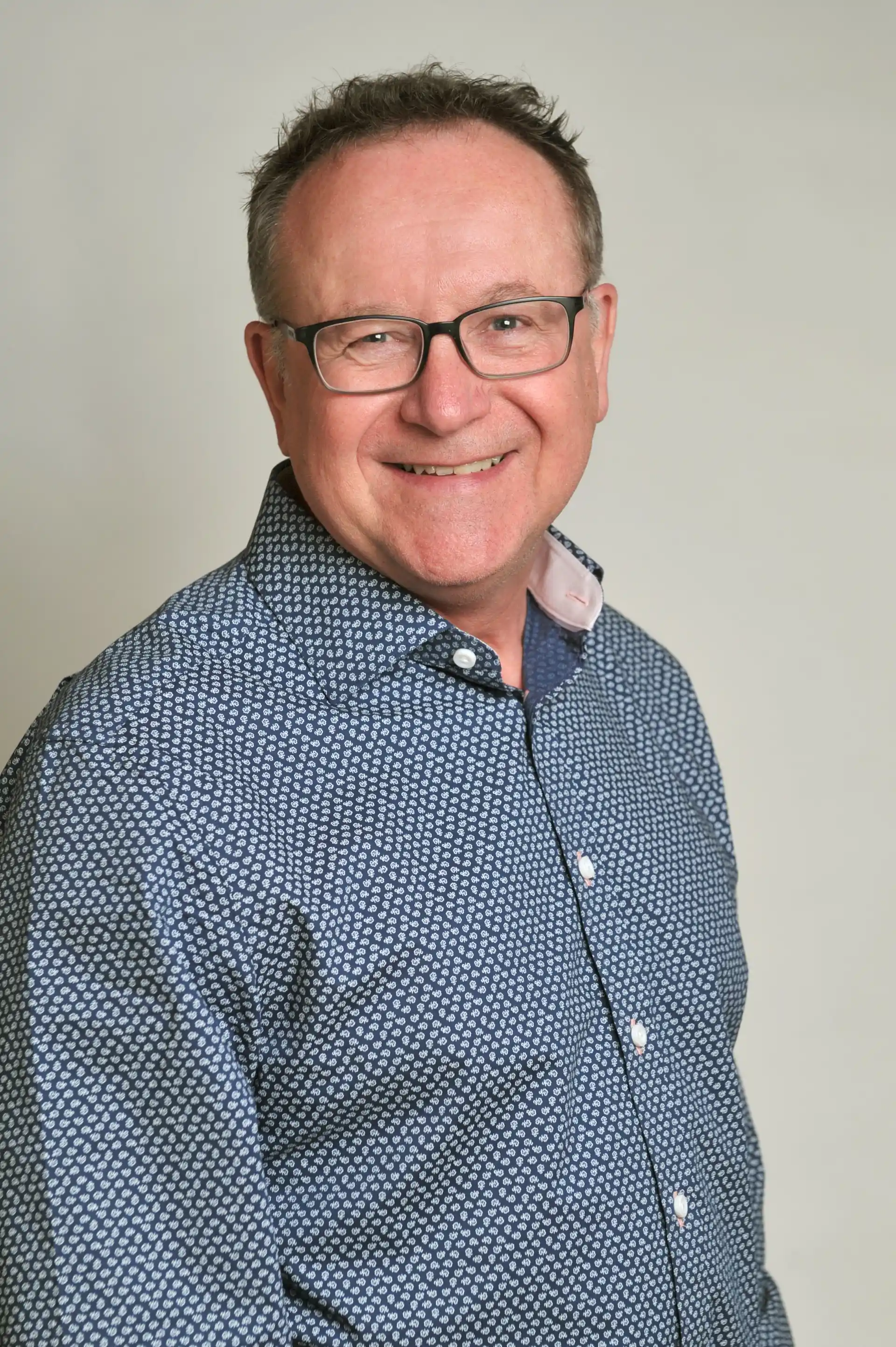 Danny Roberts wearing black glasses and a blue shirt smiling at camera.