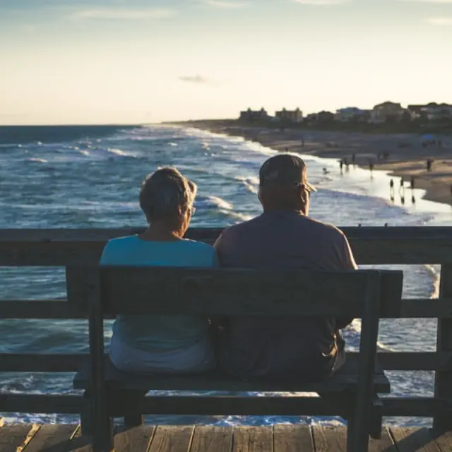 A retired couple watching the sunset from a pier above a beach.