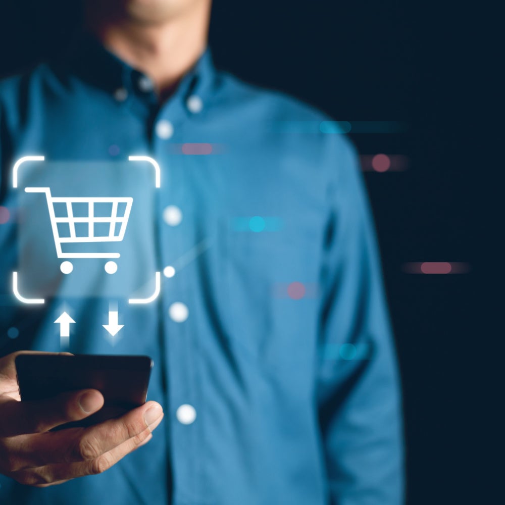 A man in a blue shirt holds a phone with a shopping cart image floating above.