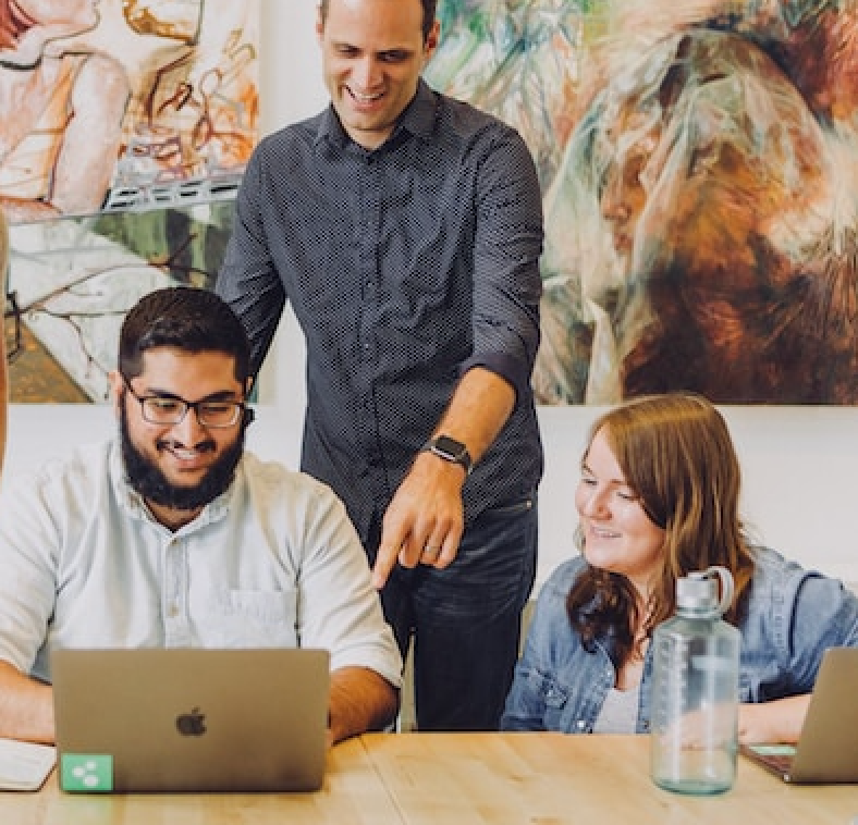 NelsonHall stock image three employees around a laptop smiling.