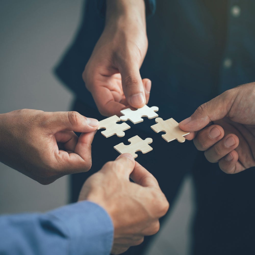 Four hands holding individual puzzle pieces connecting