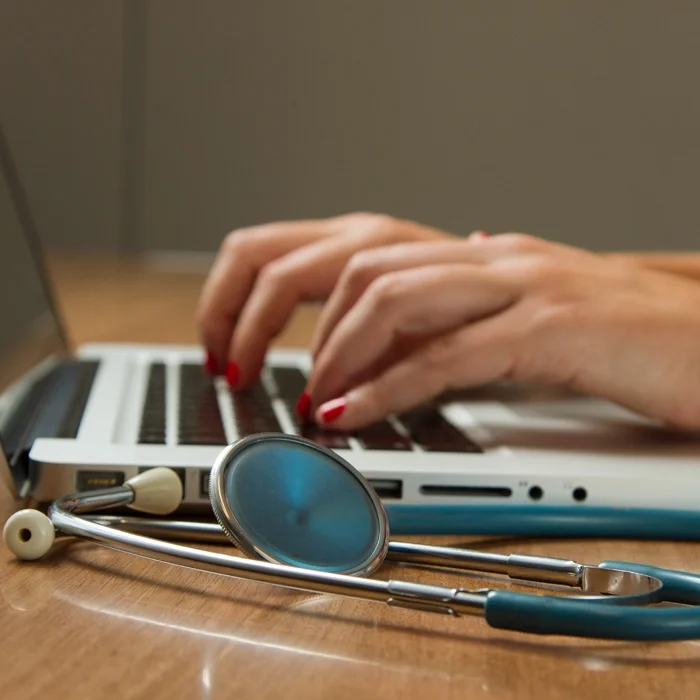 Woman typing on laptop with stethoscope 