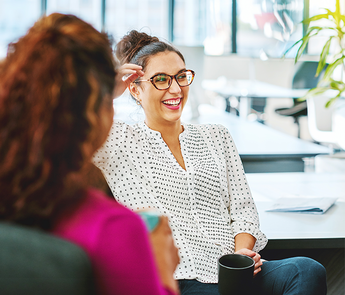 Female coworkers laughing and drinking coffee together