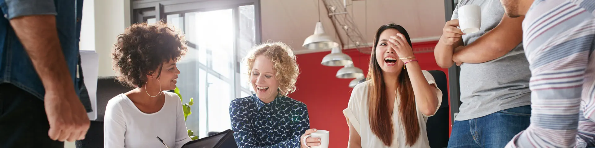 A group of coworkers laughing together in a common space of an open office.