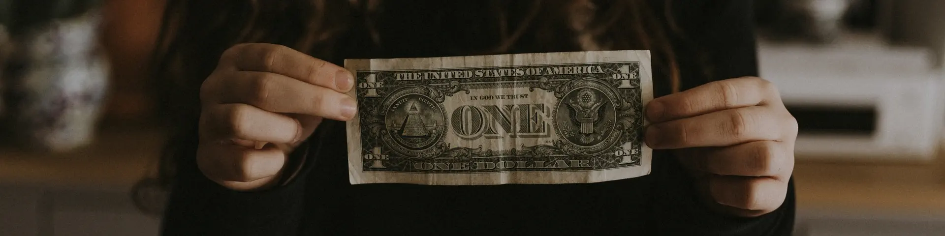 A woman holding up a "one" dollar bill.