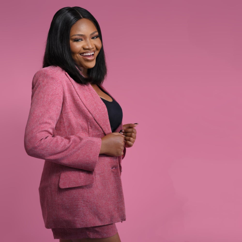 A women smiling in a pink blazer with a pink background 