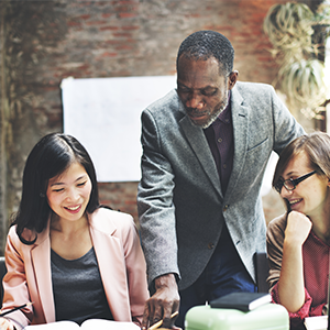 A senior coworker shares important data with junior coworkers in an open office space.