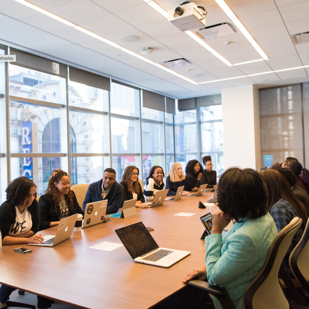A group of diverse employees meet at a large conference table. 