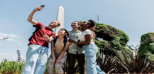 Cuatro jóvenes tomándose una selfie frente al Obelisco y los jardines verticales en Buenos Aires.