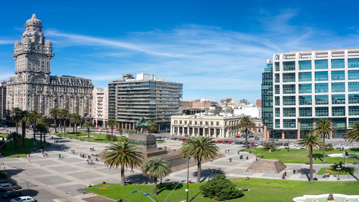 Panorámica de la Plaza Independencia en Montevideo con el Palacio Salvo y edificios modernos bajo un cielo azul.