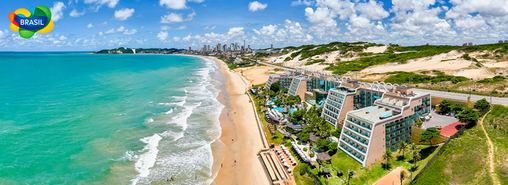 Vista panorámica de la playa de Ponta Negra en Natal, Brasil, con hoteles frente al mar, dunas y ciudad al fondo.