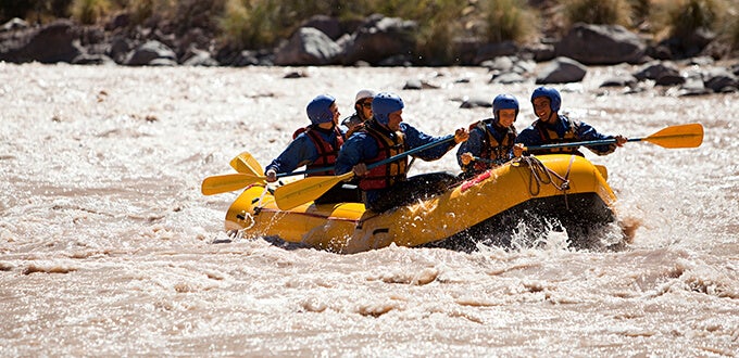 Grupo practicando rafting en balsa amarilla sobre aguas rápidas en Mendoza, disfrutando aventura y turismo activo en la naturaleza.