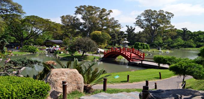 Puente rojo arqueado sobre un lago en el Jardín Japonés de Buenos Aires, rodeado de vegetación.