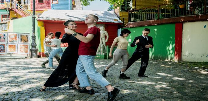 Parejas bailando tango en una calle empedrada con casas coloridas del barrio La Boca, Buenos Aires.