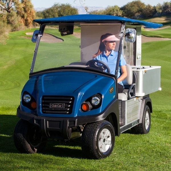 A woman drives a Club Car Cafe Express golf cart on a golf course. 
