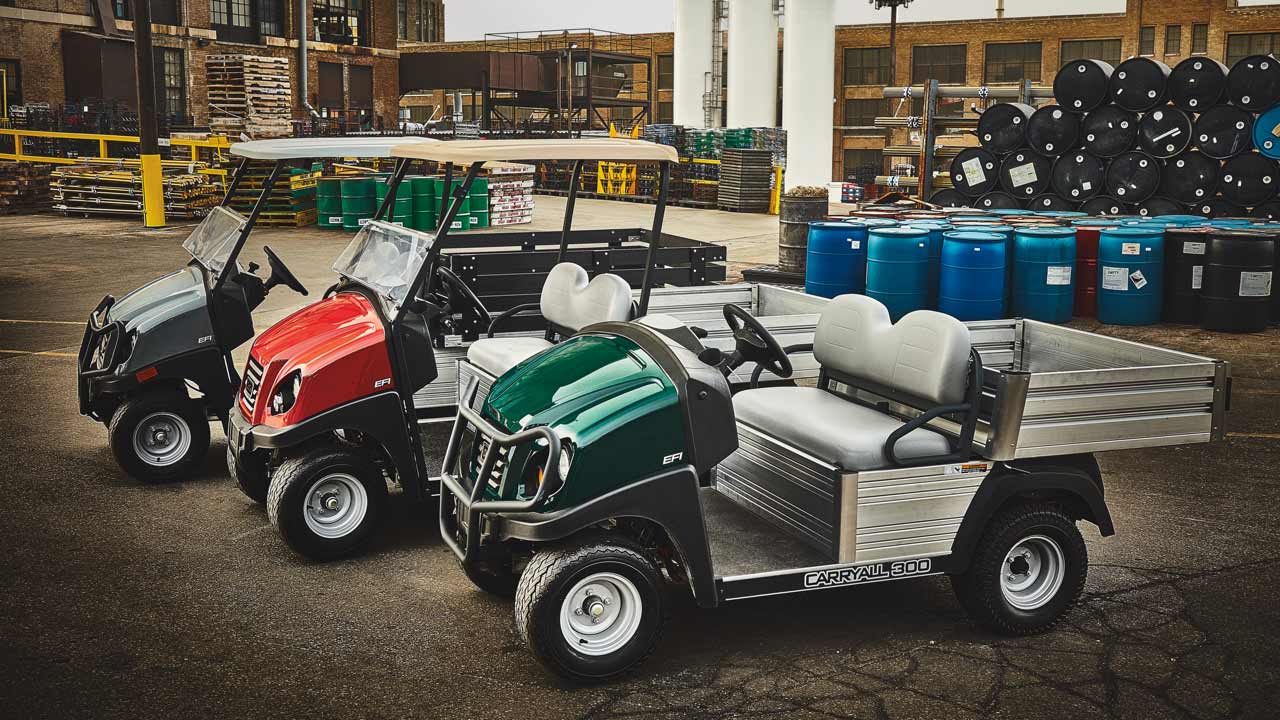 Three Club Car 4x2 utility vehicles are parked outside near a loading dock.