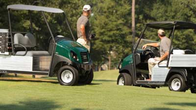 Two Club Car utility vehicles are parked outside on a golf course.