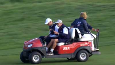 Four people drive a red Club Car with a USA flag on the side at the Ryder Cup.
