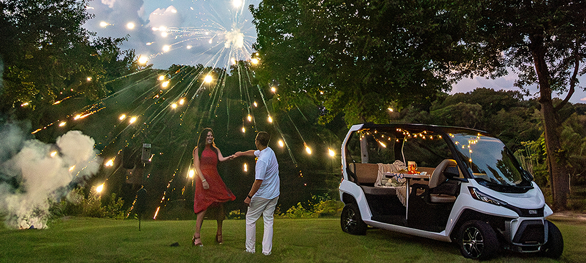A couple dances beside their Club Car CRU while fireworks explode in the night sky.