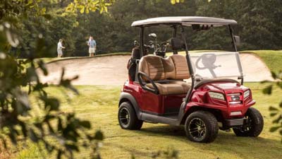 A red Club Car golf cart sits near a golf course.