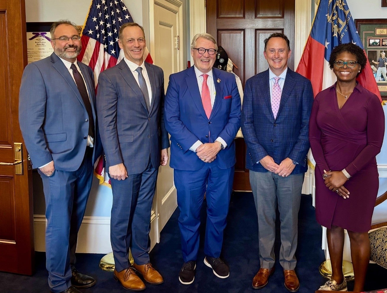 Four men and a woman in business attire, including a Club Car executive, pose together in front of the American flag in an office on Capitol Hill.