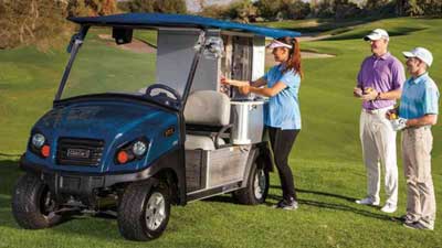 A woman pours a drink from a Club Car Cafe Express while two golfers stand waiting.