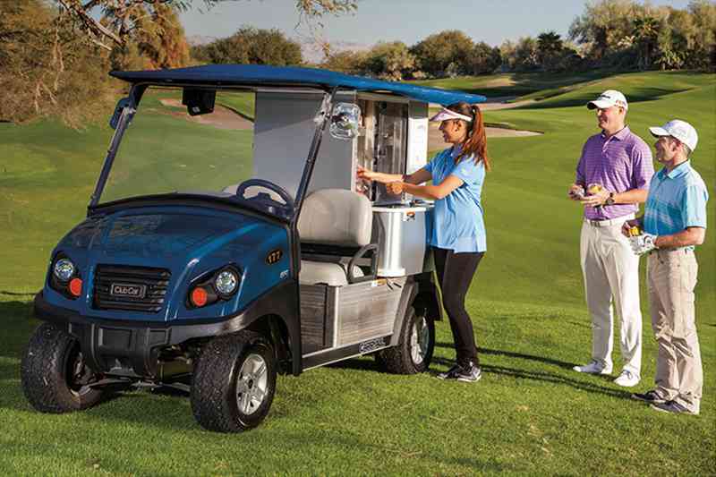 A woman pours a drink from the Cafe Express while two men stand next to the cart on the golf course.