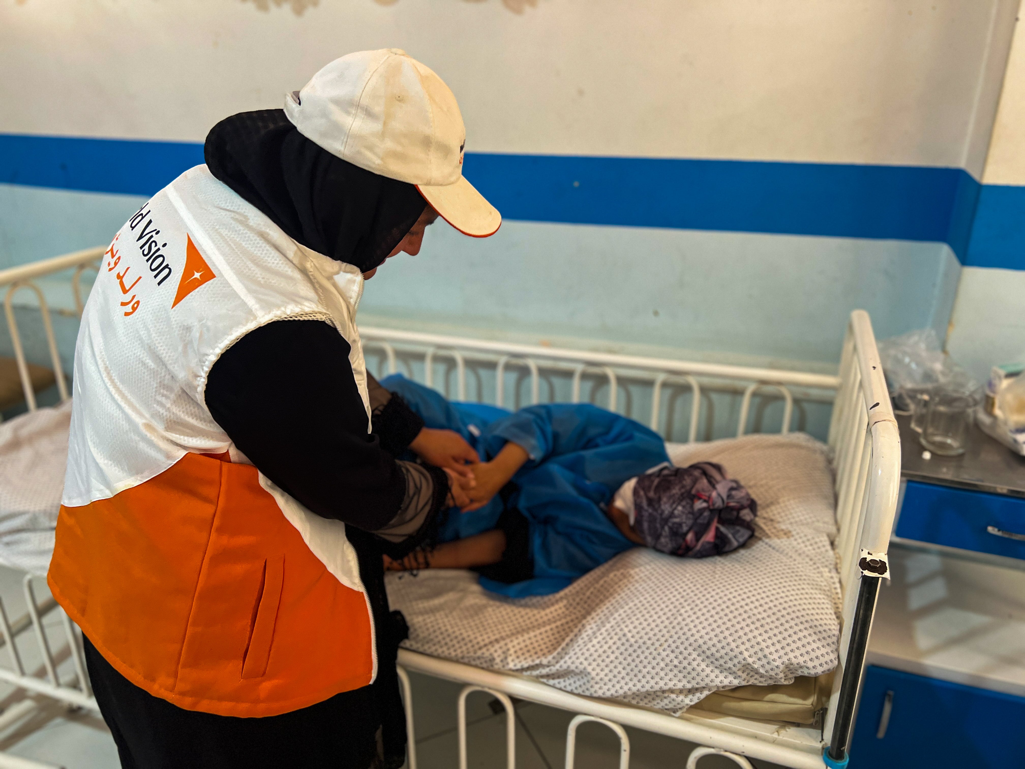 A World Vision staff member helps a patient laying on a bed in a health clinic