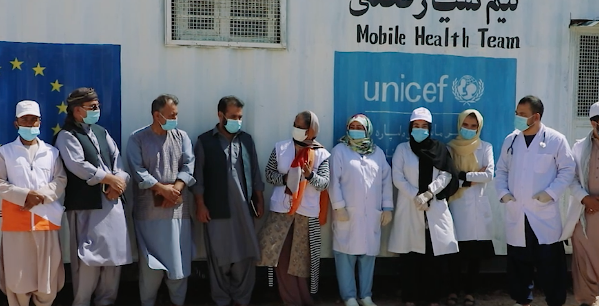 A group of people wearing surgical masks standing side by side in front of a container truck. 