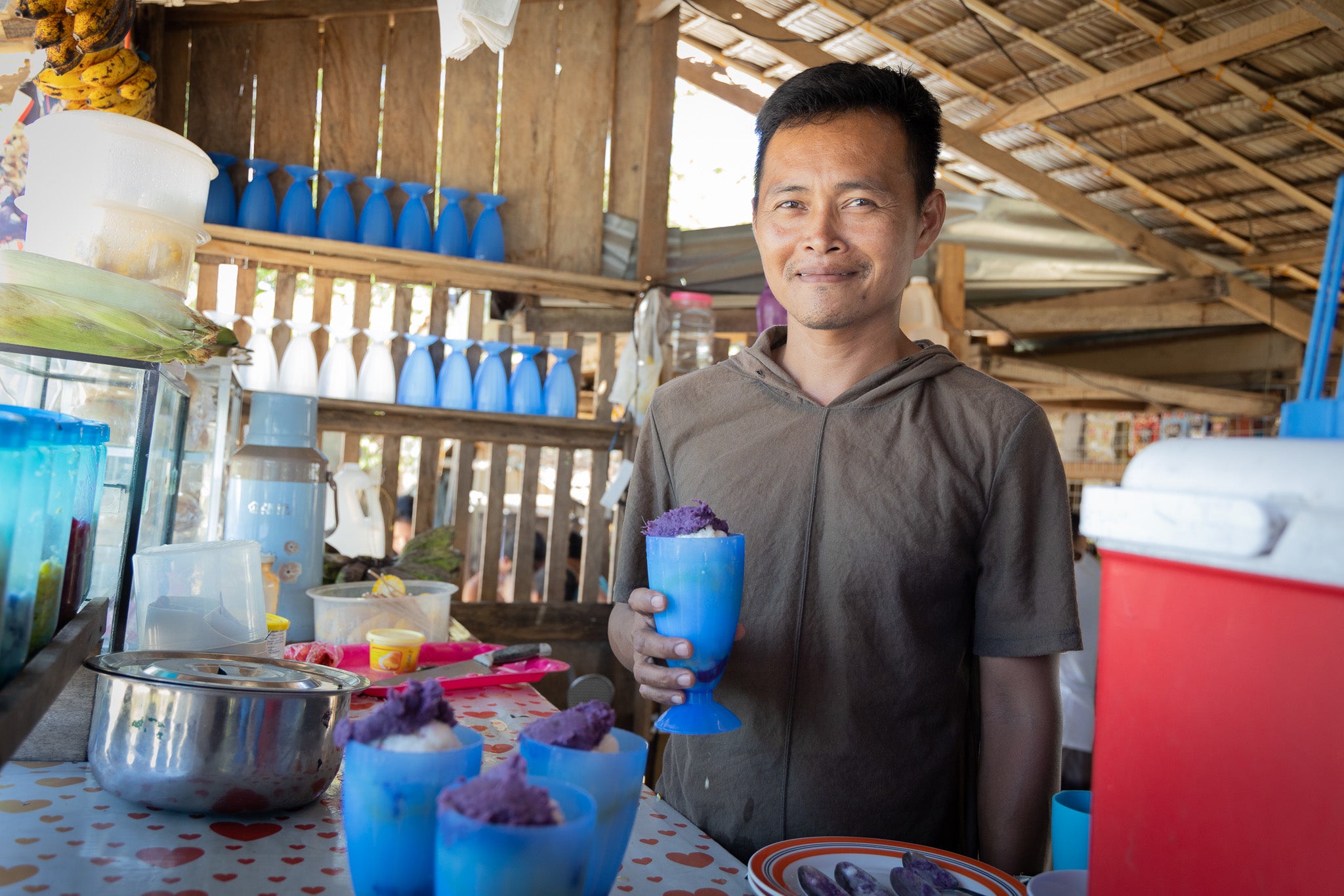 A man stands in his shop smiling while holding a cup of Halo-Halo, a famous dessert in the Philippines. 