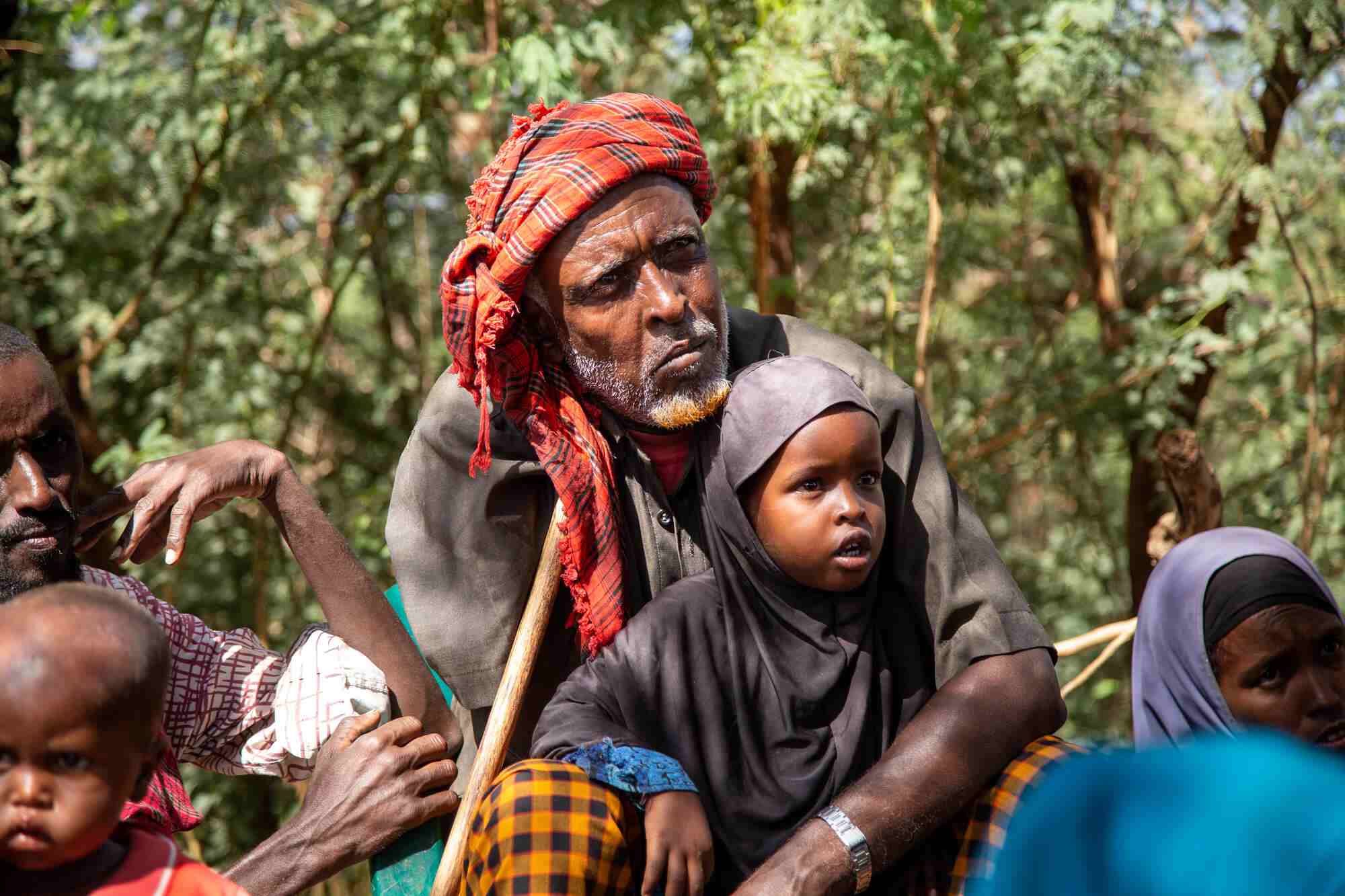 In an Internally Displaced Persons camp in Somalia, a man sits within a group of people with a toddler on his lap. 
