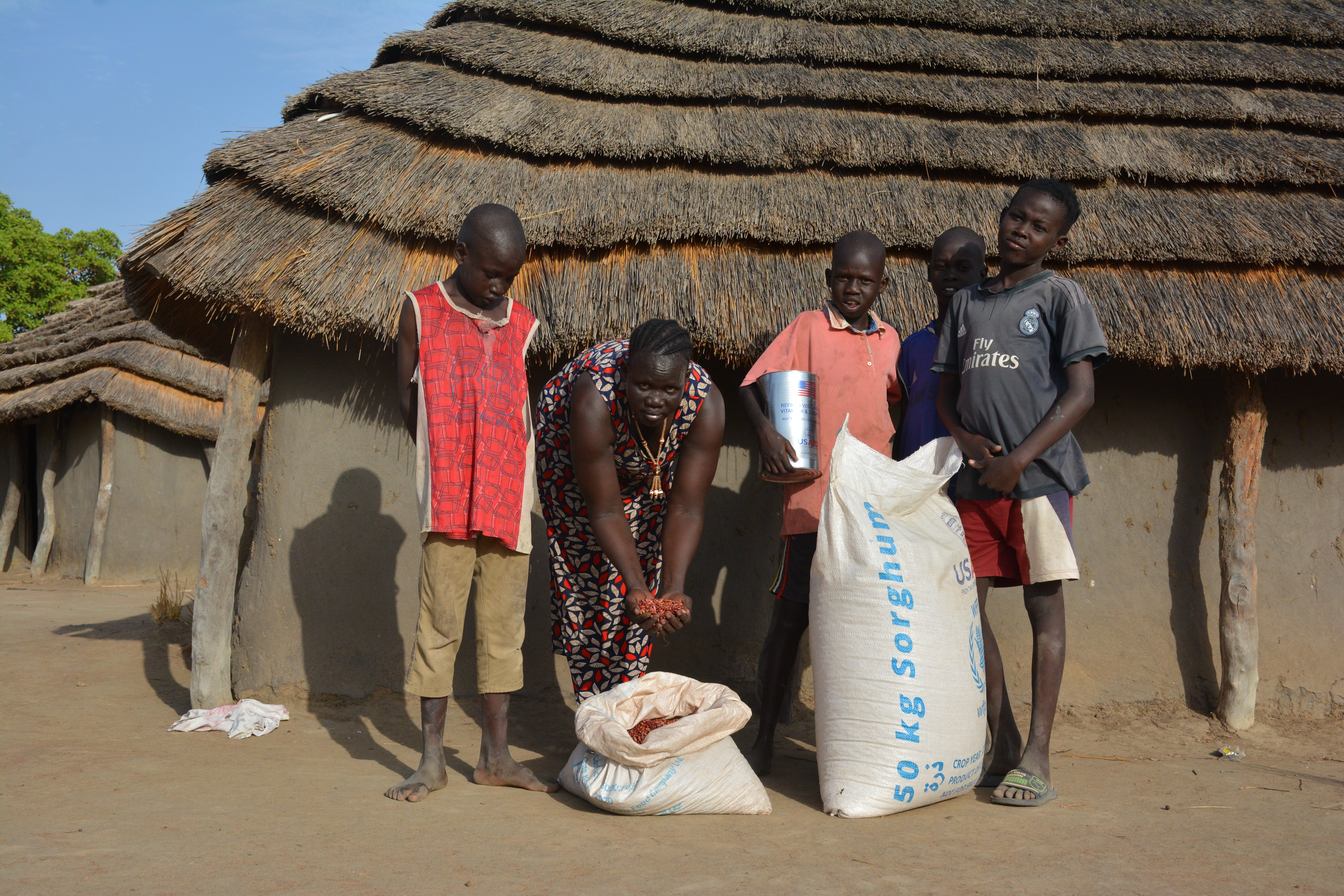 A family of five standing outside of a dwelling with two bags of flour.