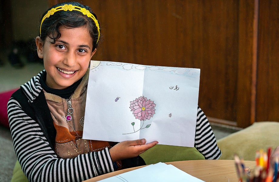A girl showing off her drawing of a pink flower.