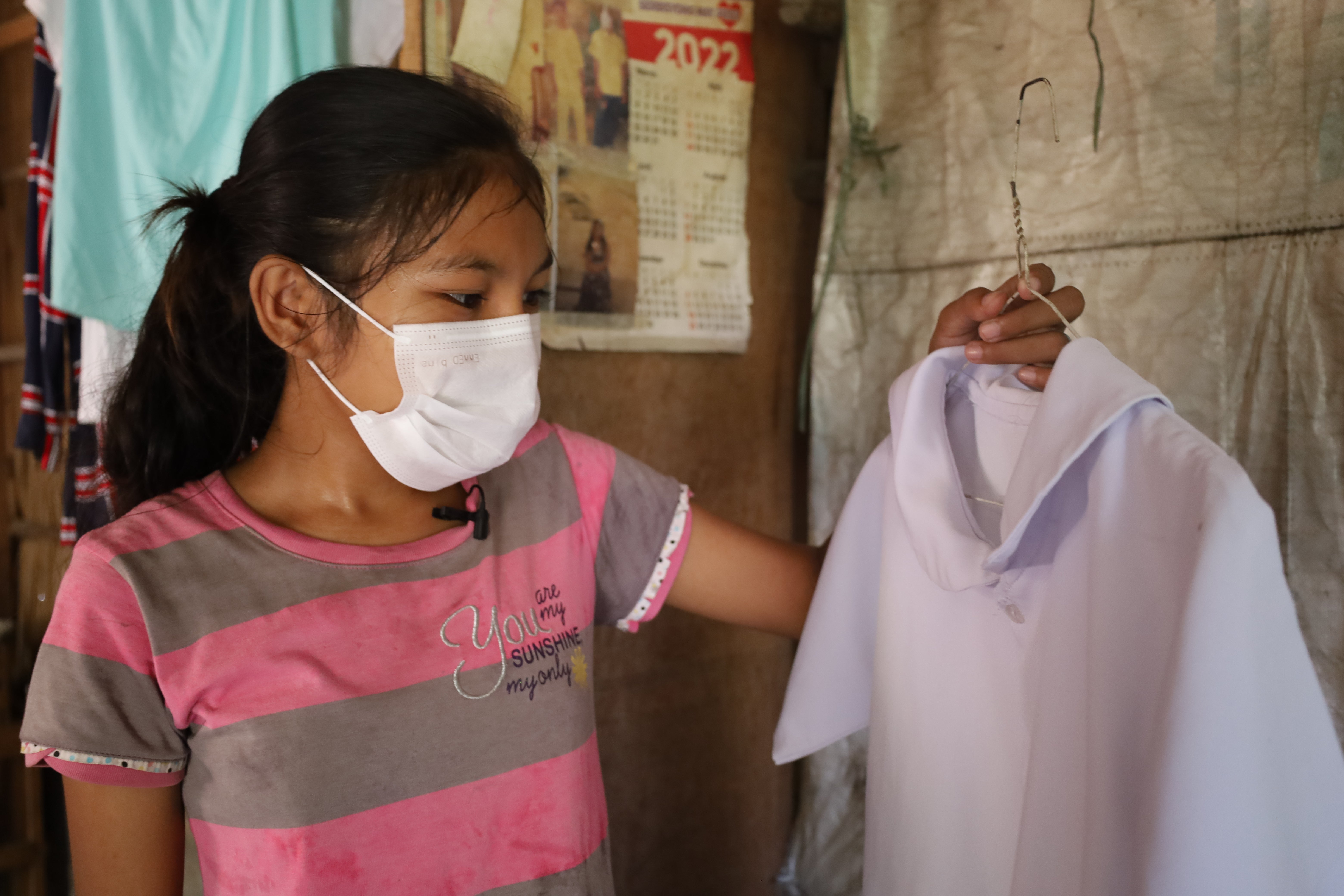 In the Philippines, a young girl wearing a mark looks at her school uniform. 
