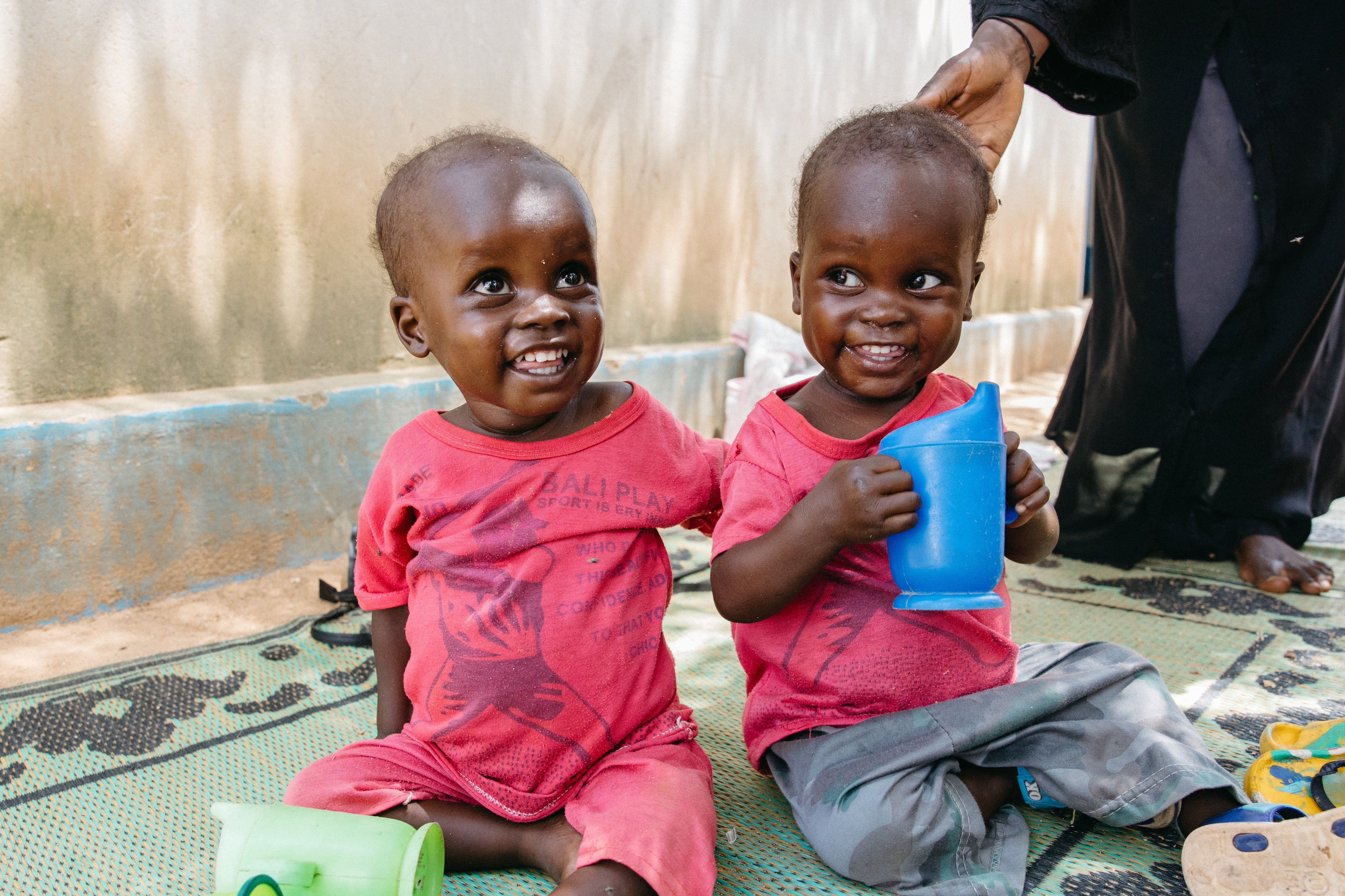 Two beautiful recovering twin brothers sit up and smile at the camera.