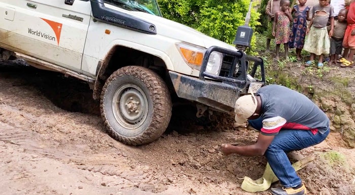 A man attempting to lift a World Vision vehicle out of a muddy area.