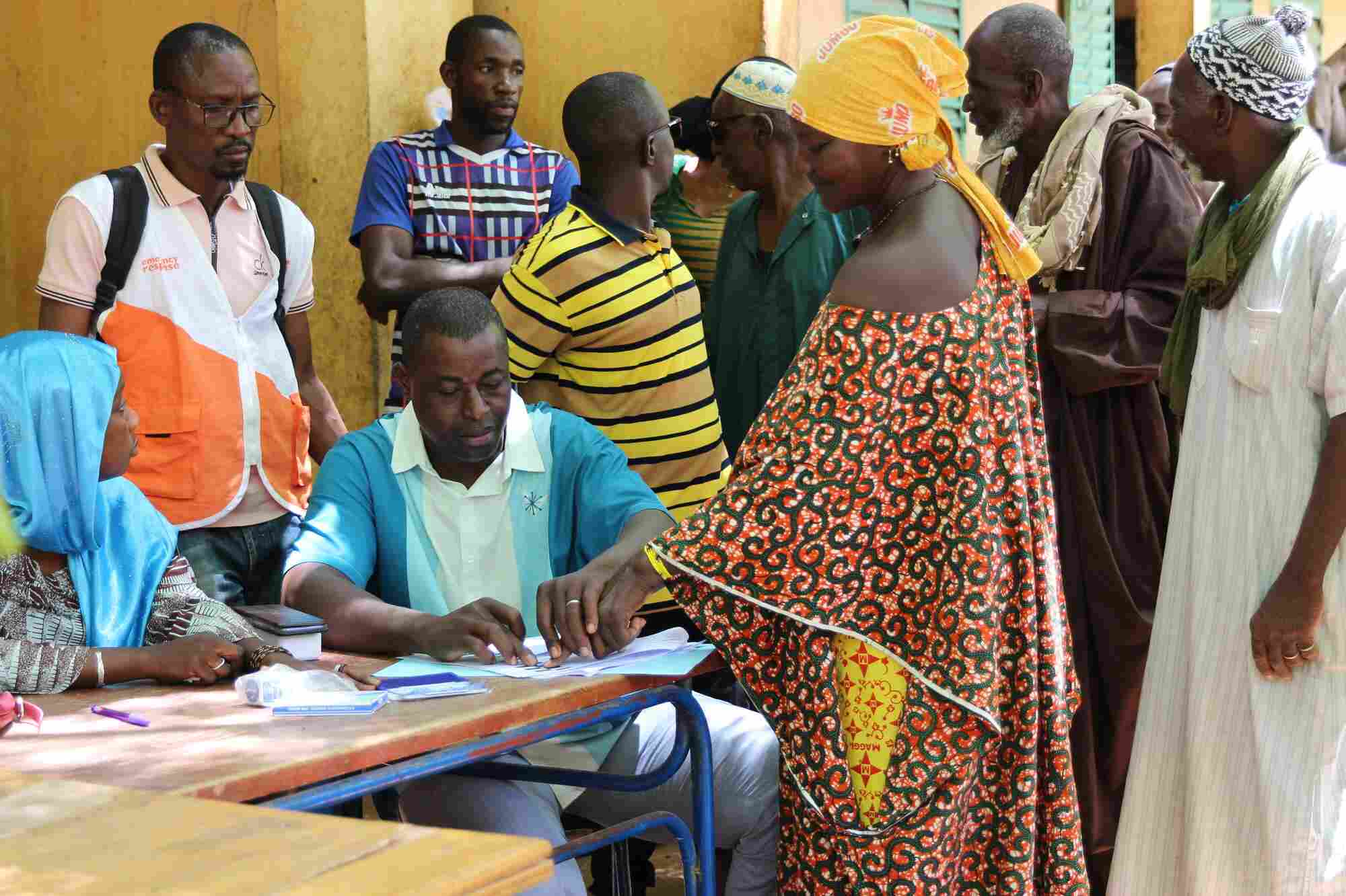In Mali, World Vision staff assist local community members to receive their cash distribution at a table.