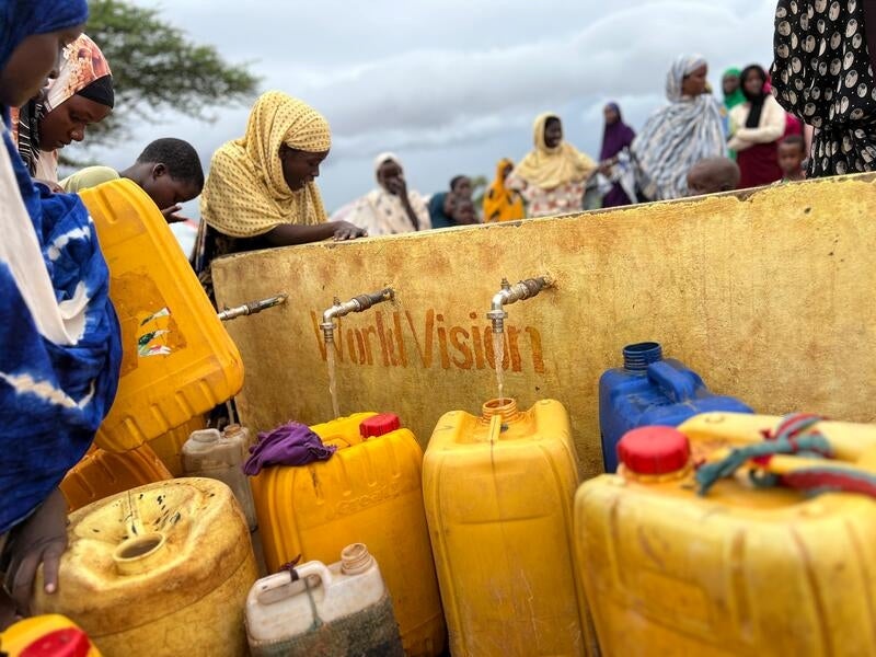 In Somalia, water with a slight orange colouring pours from a water source into yellow jugs.