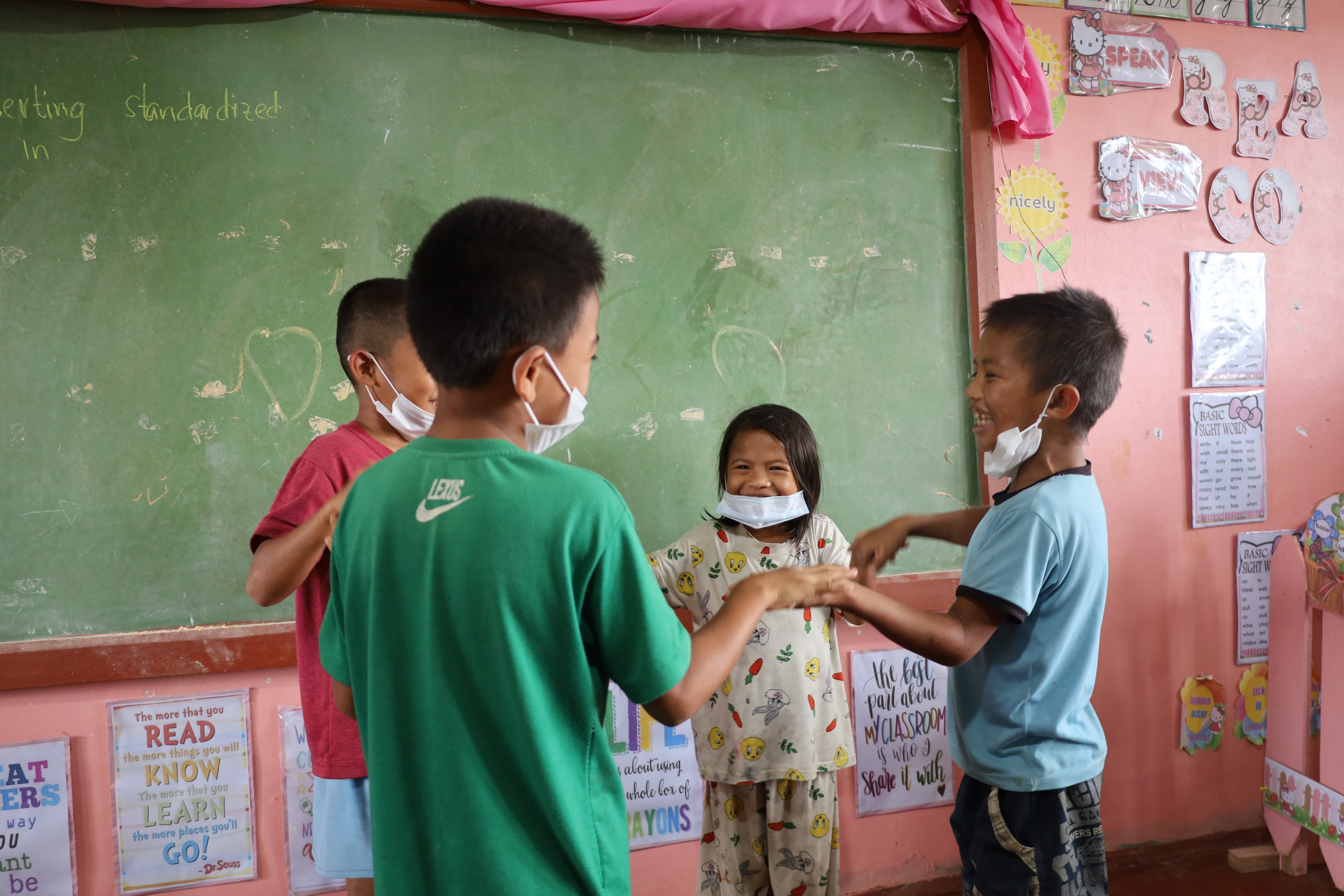 In the Philippines, four children smile and hold hands in a circle inside an education center