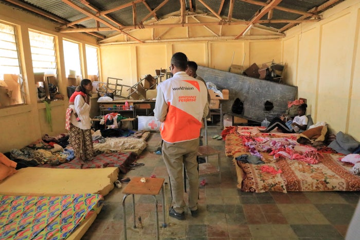 A World Vision staff standing inside a temporary shelter with mattresses laid out on the floor.
