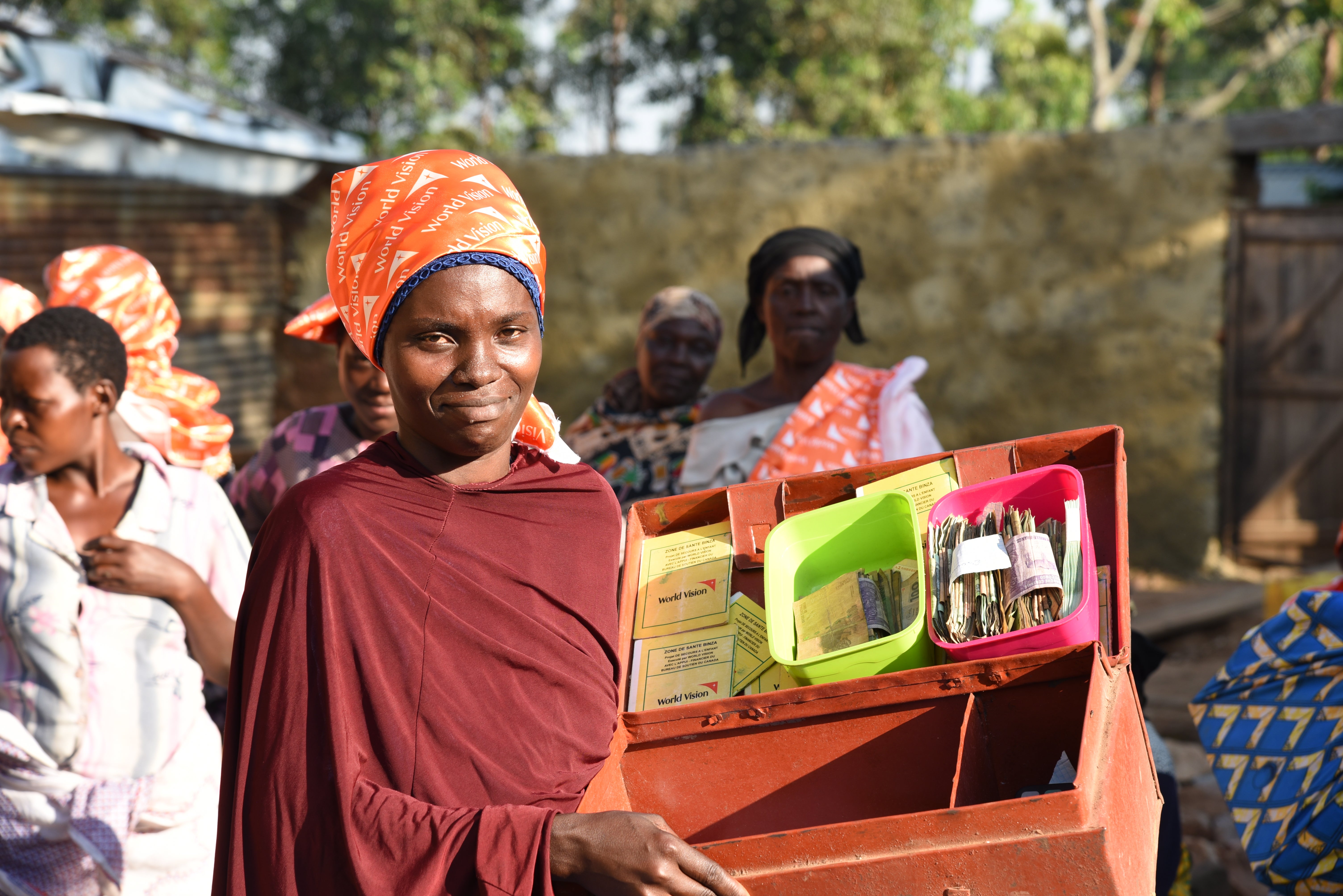 A women smiles as she holds open a box she uses for her savings plan.