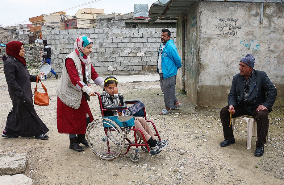 A woman pushes a girl in a wheelchair while three other adults look on.